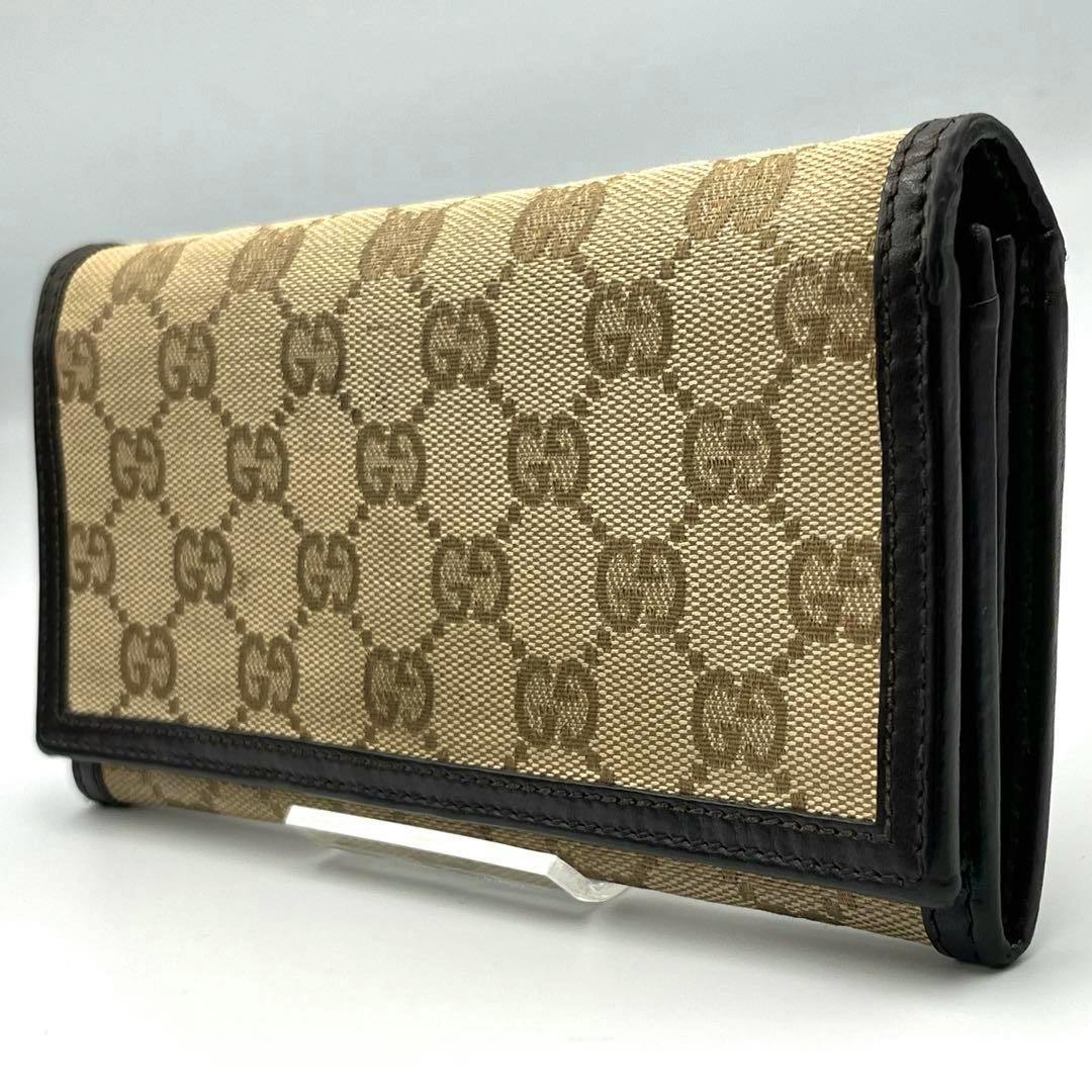 Angled photo of a beige Gucci canvas bi-fold long wallet with GG monogram and dark leather trim.
