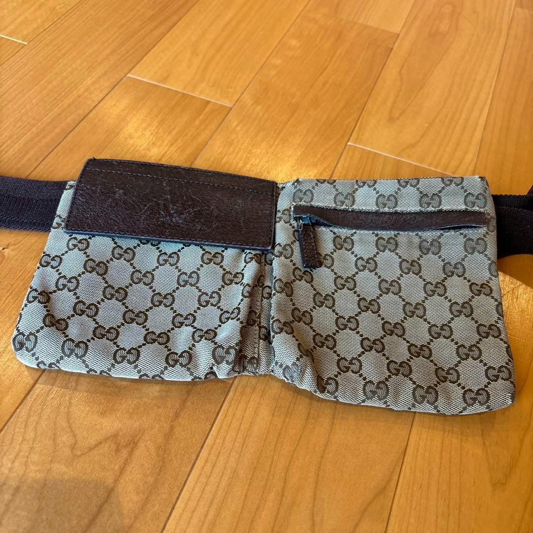 GUCCI GG canvas waist pouch (body bag) laid open on a wooden floor showing two compartments and its strap.