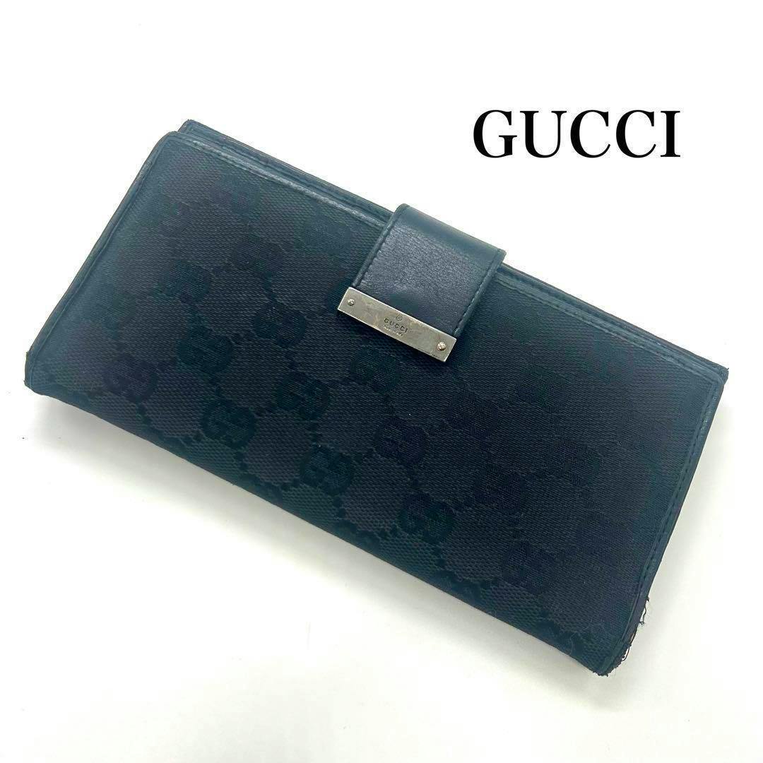 Black GUCCI GG canvas long wallet with front strap, metal logo plate, shown on a white background.