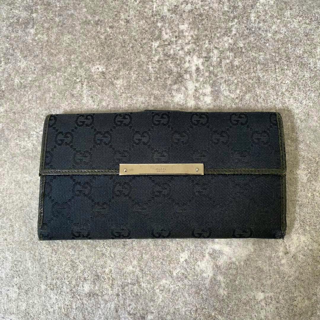 Black Gucci GG canvas long flap wallet shown flat with a rectangular metal logo plate on the front.