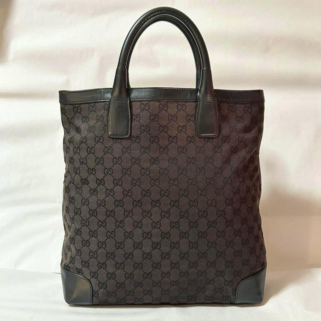 Front view of a black Gucci GG canvas tote bag with leather handles and leather-reinforced corners.