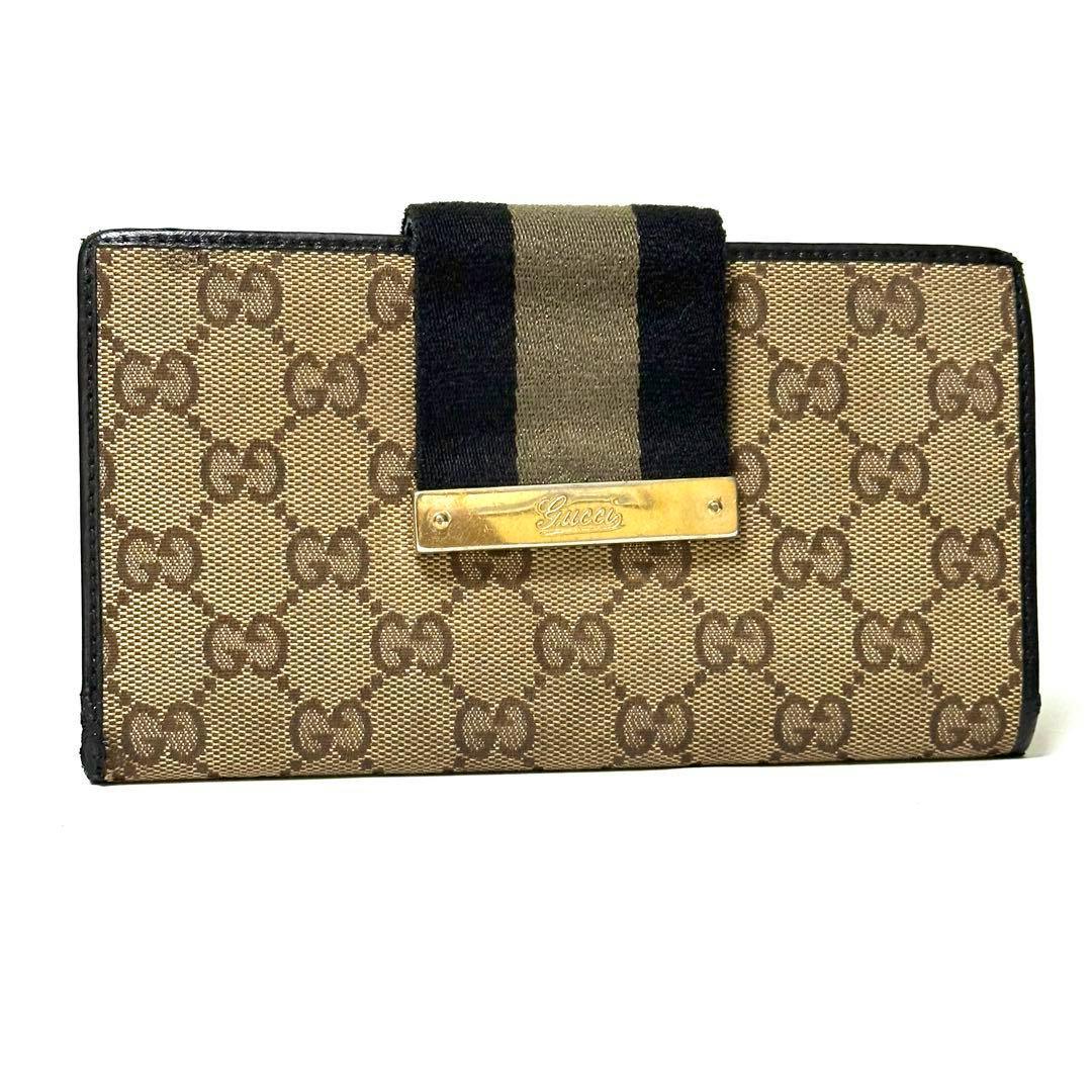 Front view of the GUCCI long canvas wallet with GG pattern, black trim, fabric strap, and a gold metal Gucci logo plate.