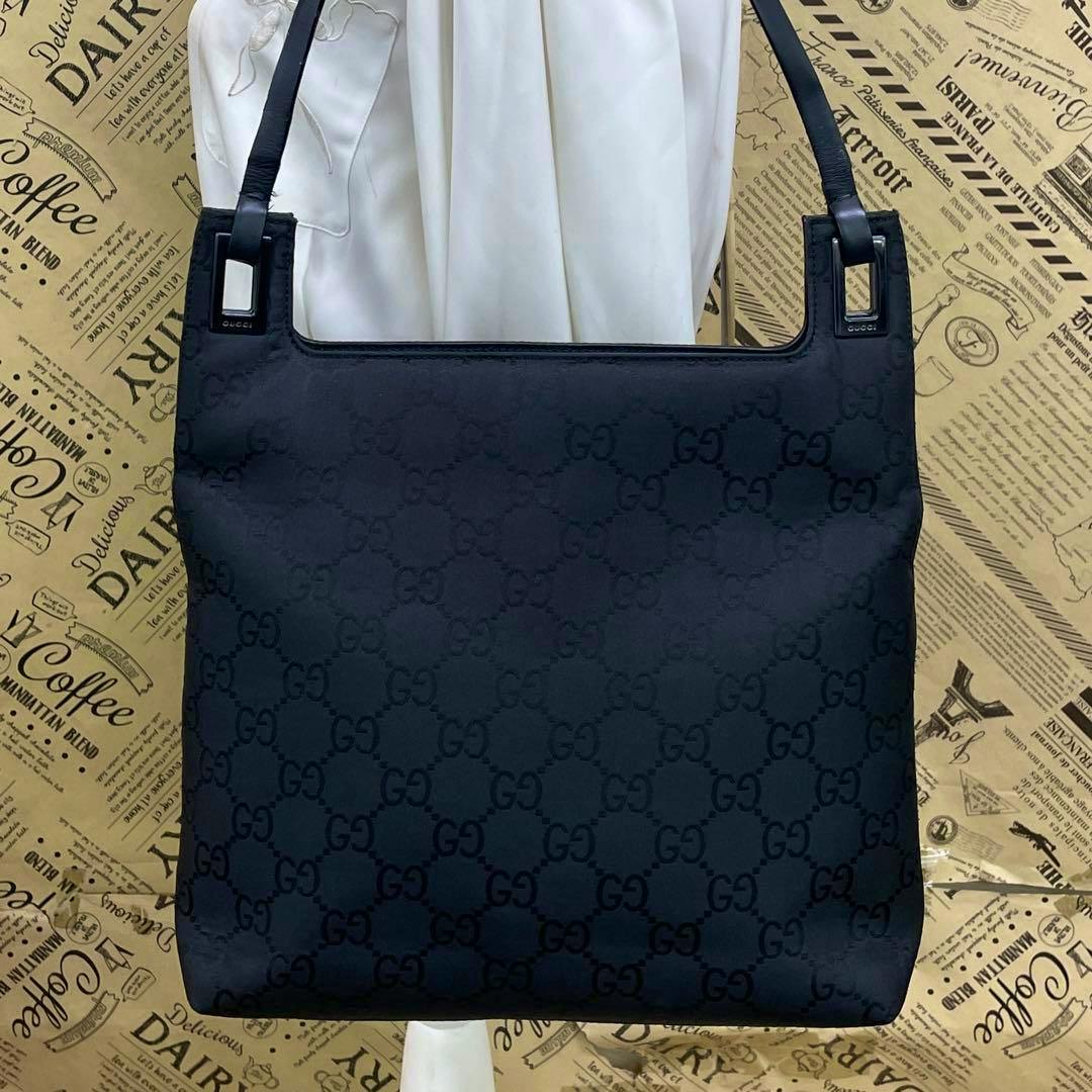 Front view of a black Gucci GG canvas one-shoulder handbag hanging on a display.