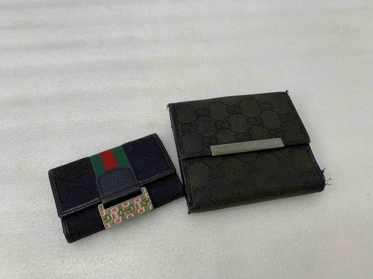 Two GUCCI items — a GG canvas bifold wallet and a GG canvas key case with green-red web stripe — shown on a white surface.