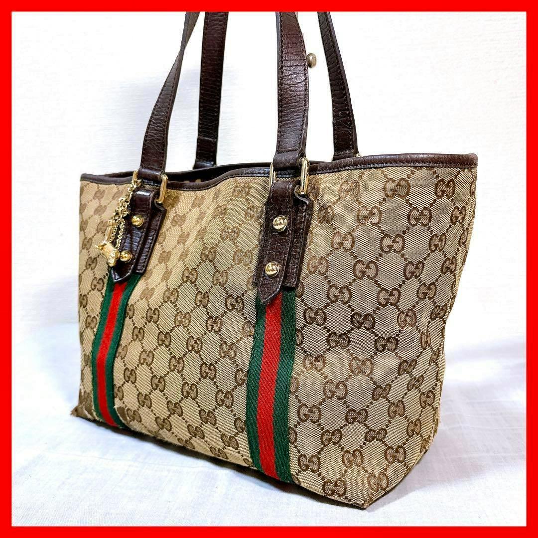 Three-quarter view of a brown Gucci GG canvas tote bag with brown leather handles and green-red-green web stripe.