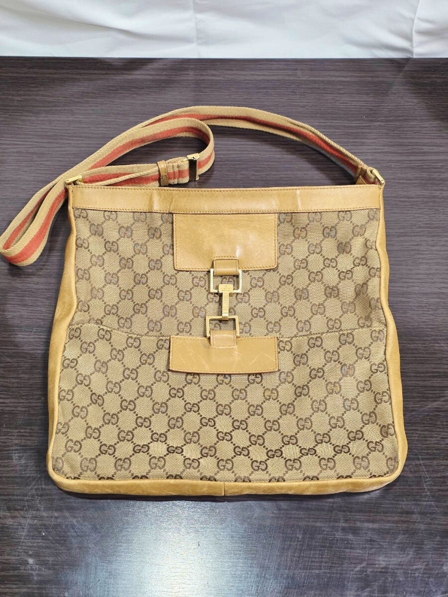 Front view of the Gucci GG canvas beige shoulder bag with leather trim, striped shoulder strap, and front buckle detail.