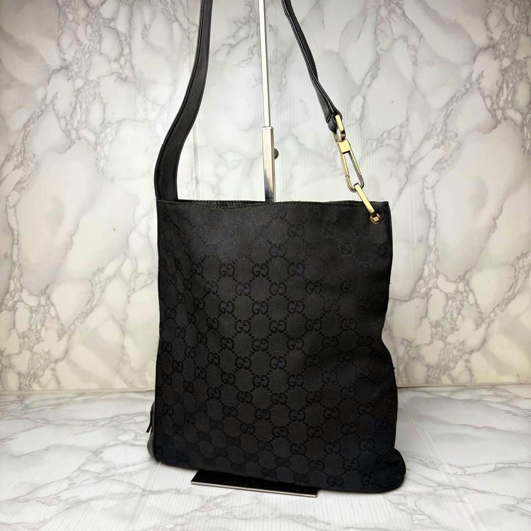 Black GUCCI GG canvas shoulder bag hanging on a stand, front view showing leather strap and gold hardware.