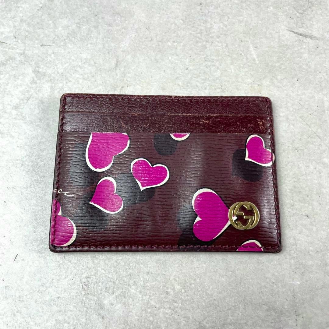 Bordeaux leather PVC Gucci card case with pink heart print and a small gold GG logo, front view.