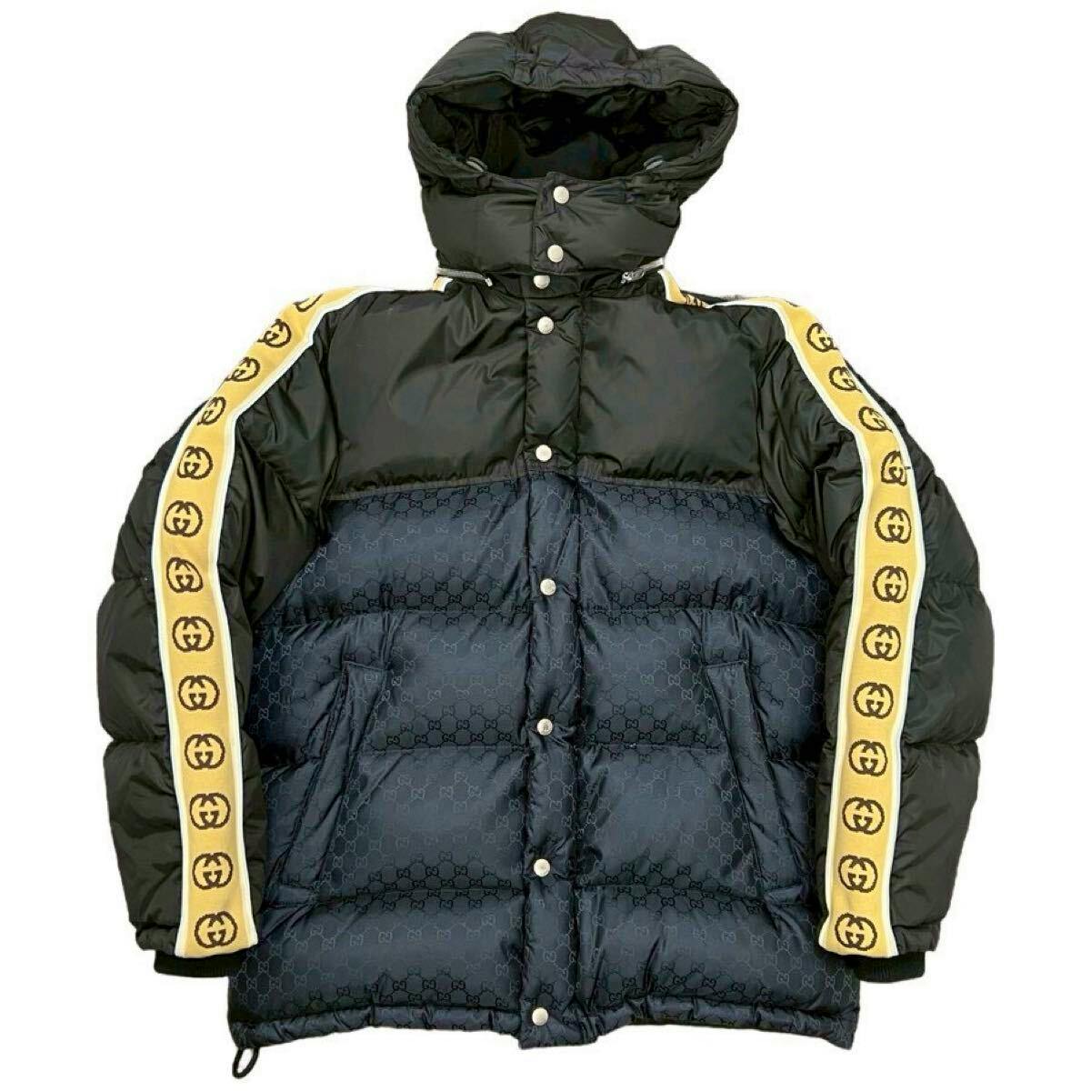 Front view of the men's Gucci nylon down jacket showing black and beige panels with GG jacquard on the body, yellow GG logo trim along the sleeves, and a detachable hood.