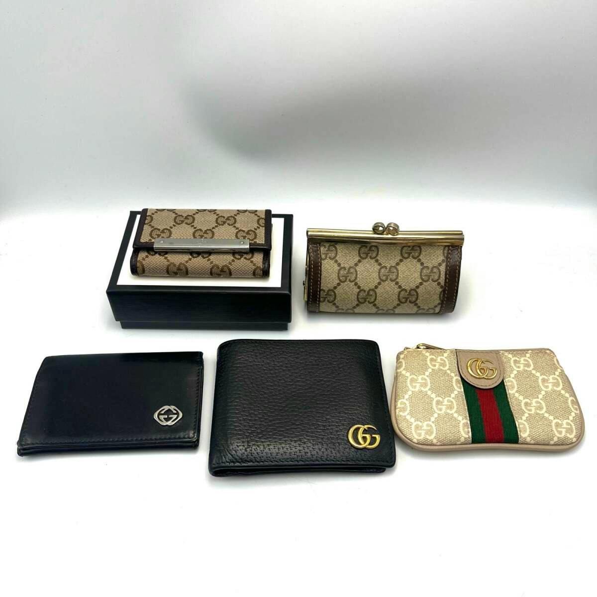 Five Gucci items including GG monogram wallets, a black leather bifold wallet, and a small GG coin pouch arranged on a white background.