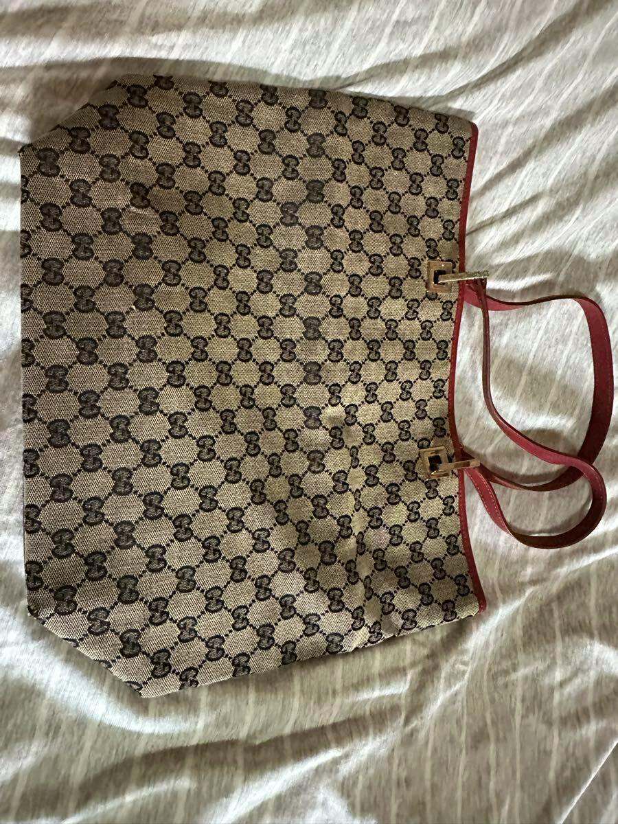 A GUCCI canvas tote bag with GG monogram pattern and red leather handles and trim laid flat on a light surface.