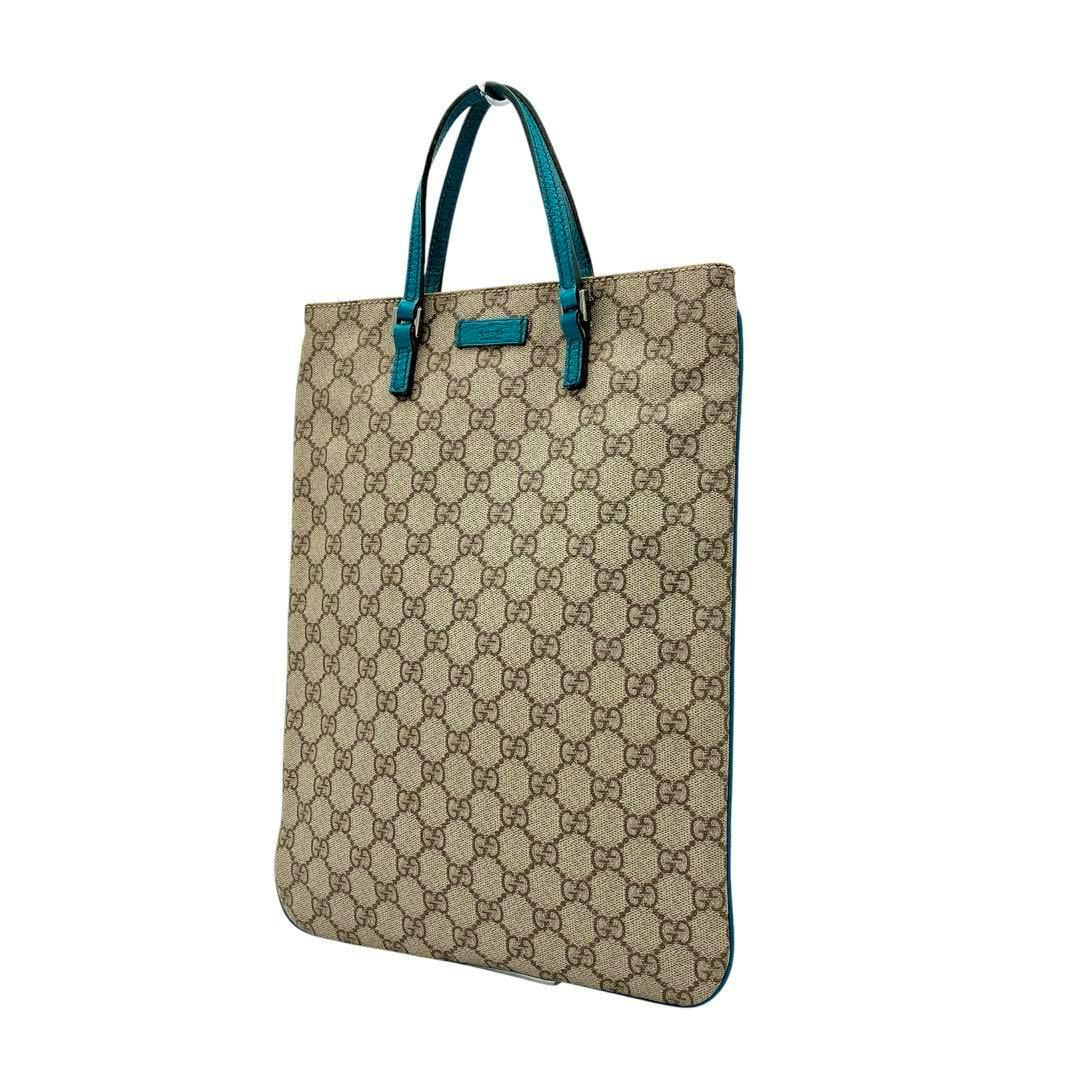 Gucci GG Supreme brown PVC tote bag with turquoise-blue handles and trim on a white background.