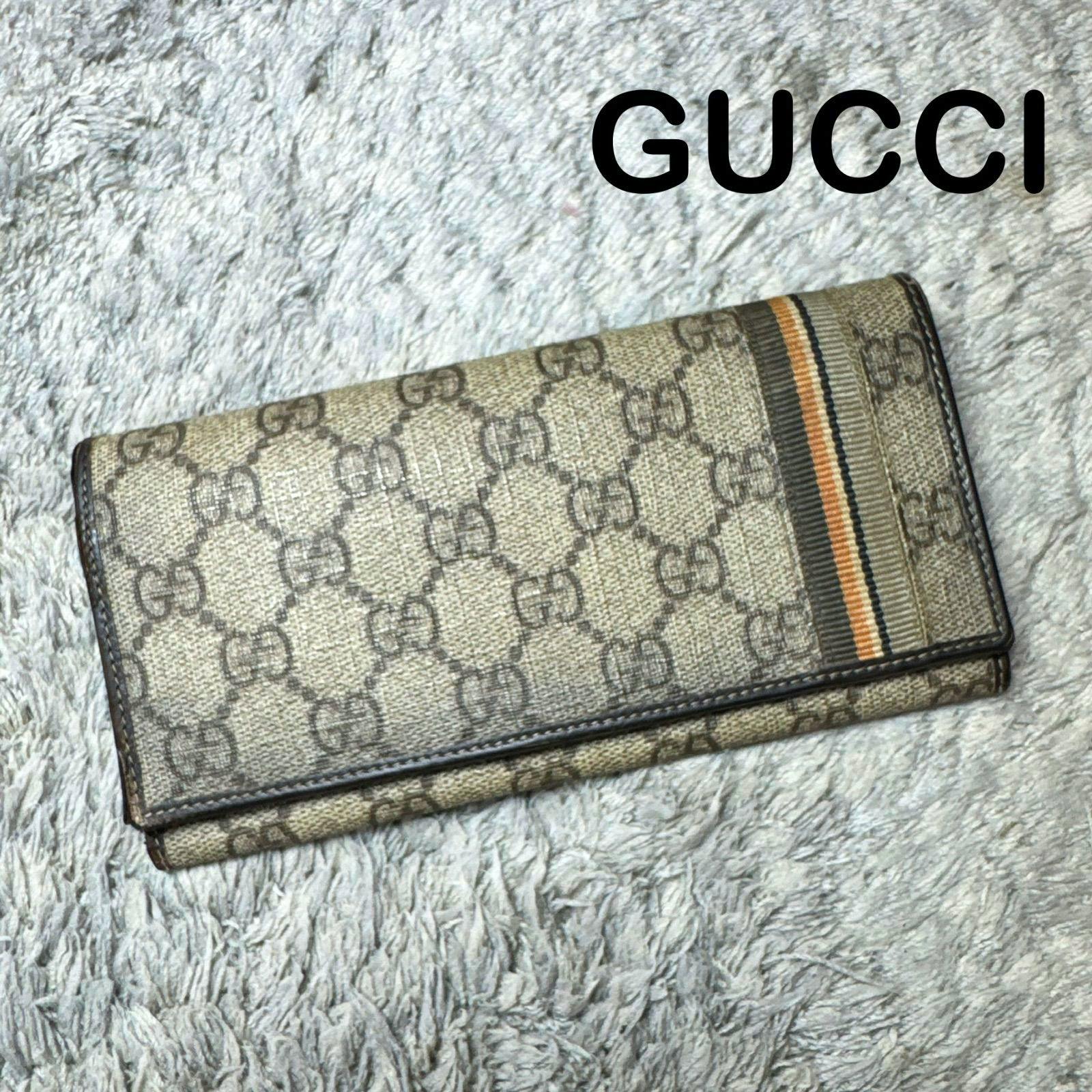 Brown GUCCI GG Supreme long flap wallet with striped webbing photographed on a light textured background.