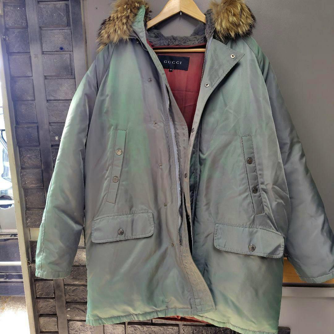 Green men's down jacket with fur-trimmed hood hanging on a hanger, front view showing pockets and partially open zipper.