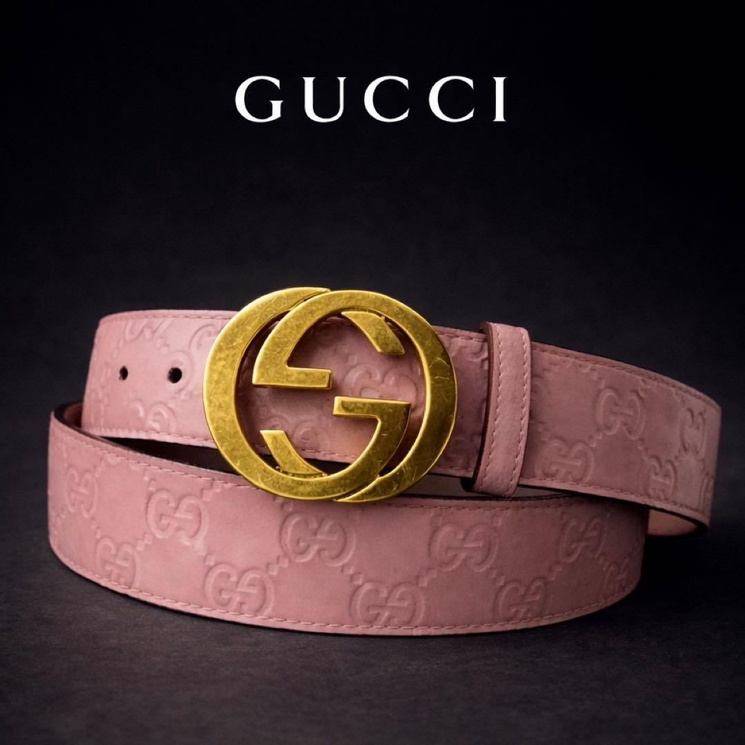 Pink Gucci leather belt with embossed GG pattern and a gold interlocking G buckle on a dark background.