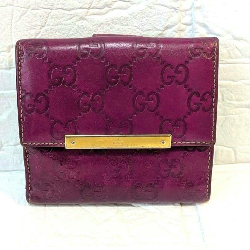 Front view of a purple leather folded wallet with embossed GG pattern and a gold-tone rectangular plaque.