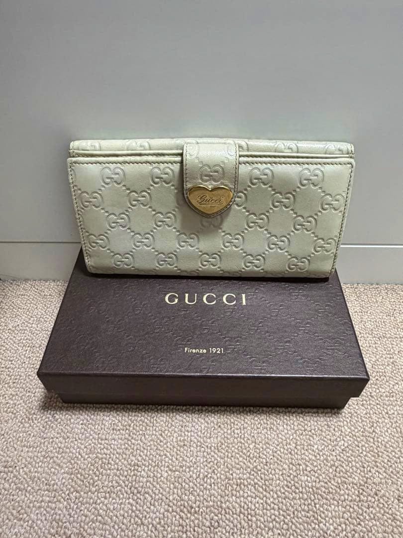 A Gucci long wallet in embossed GG leather with a heart-shaped logo plaque displayed on a Gucci box.
