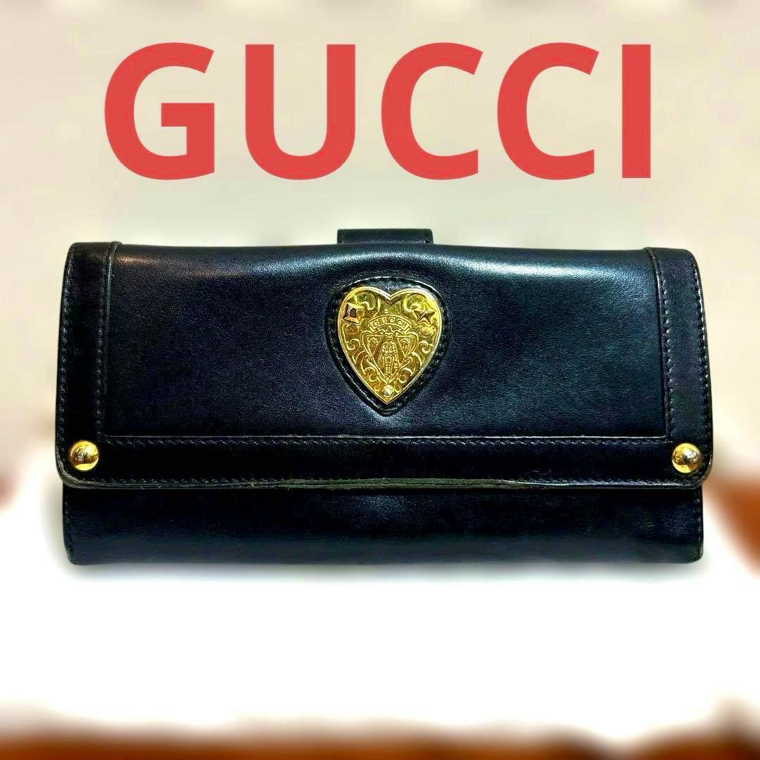 Closed black leather long wallet with a gold heart motif on the front, shown with red GUCCI text above.