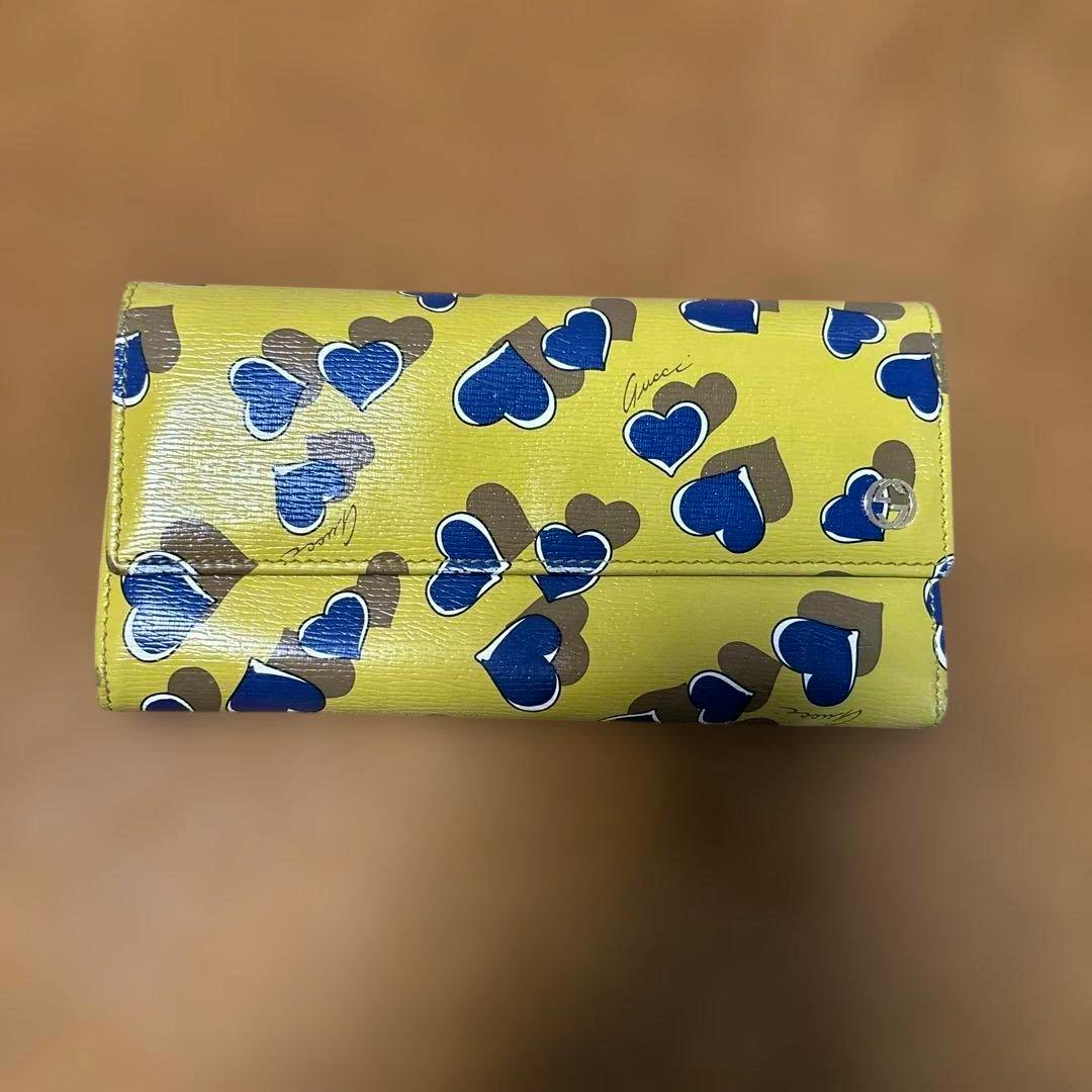 Yellow Gucci canvas long wallet with blue and brown heart pattern shown closed on a brown background.