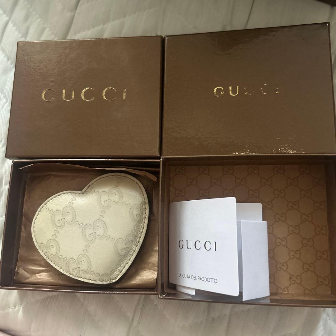 Heart-shaped Gucci leather case with monogram inside an open Gucci box alongside a Gucci booklet.