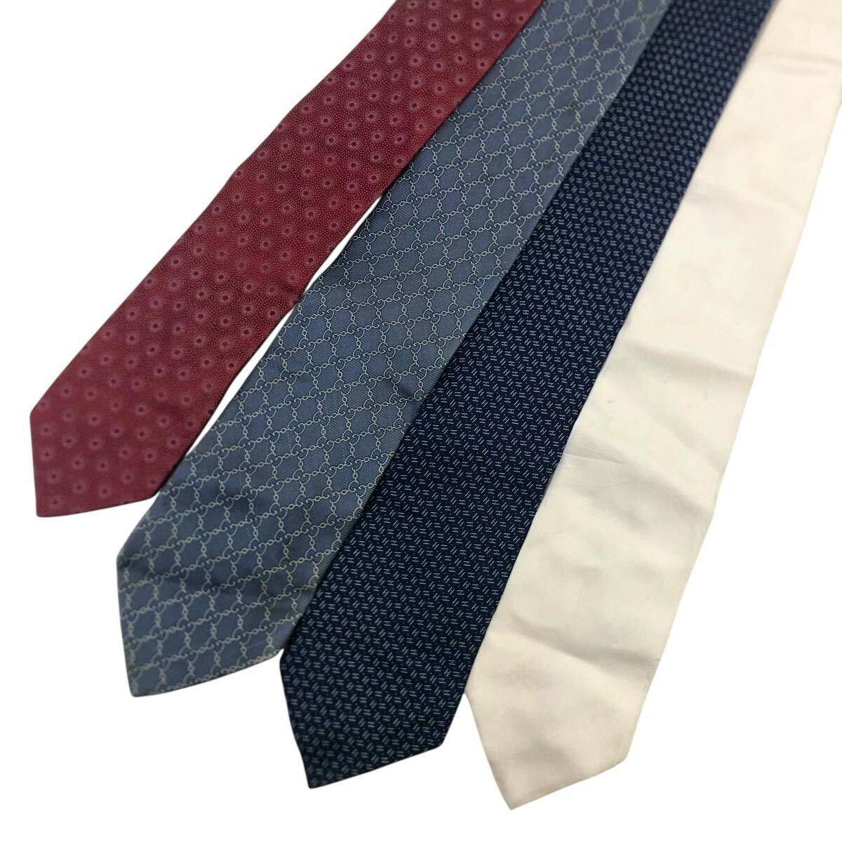 Four neckties laid side by side on a white background showing a red tie, a light gray patterned tie, a dark blue patterned tie, and a cream tie.
