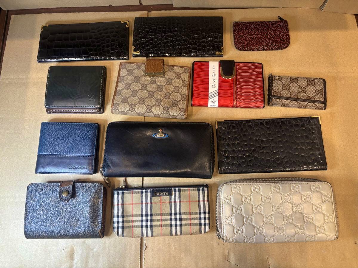 Thirteen used wallets, assorted brands including GUCCI, Louis Vuitton, and COACH, laid out on cardboard.