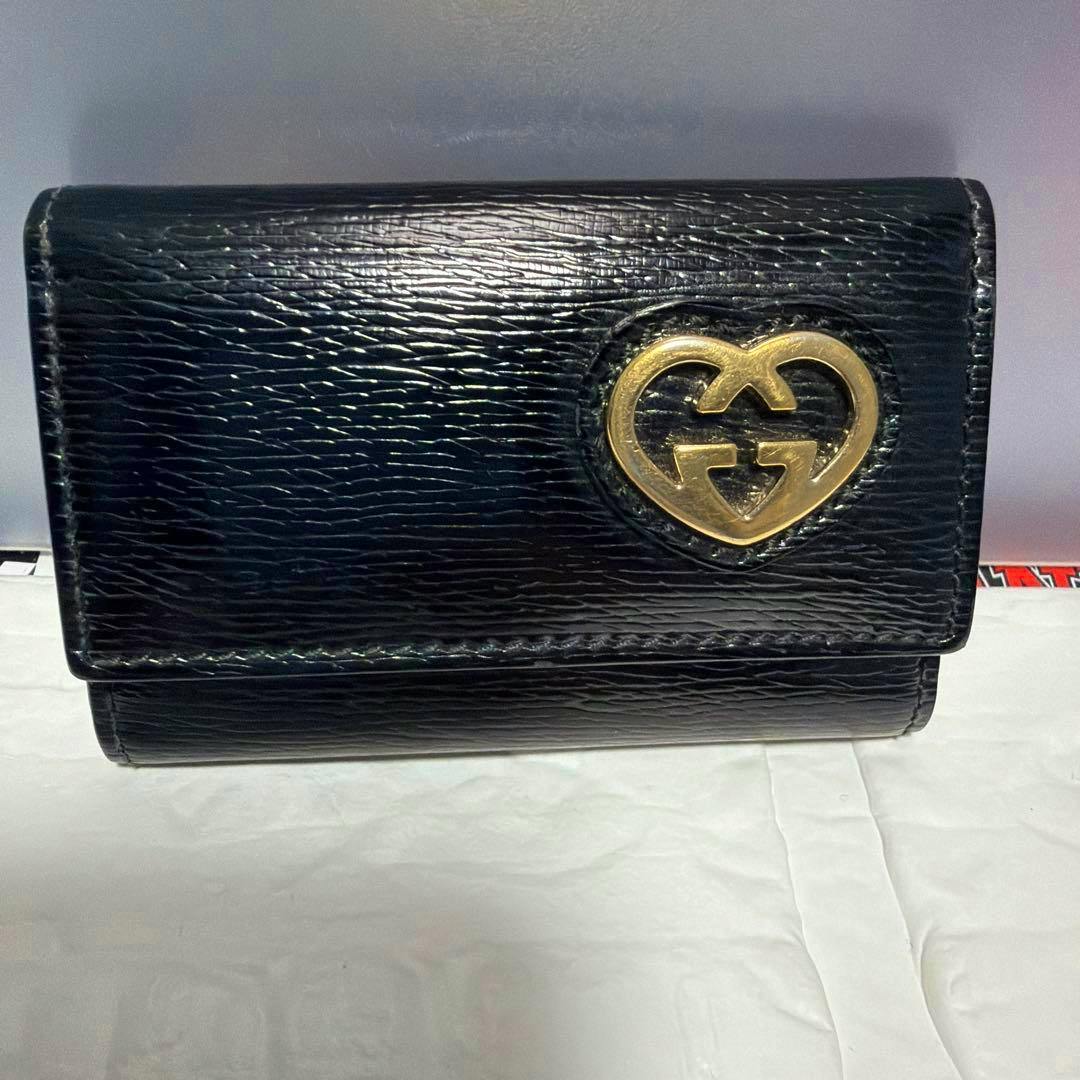 Black leather Gucci key case showing a gold interlocking G heart emblem on the front.