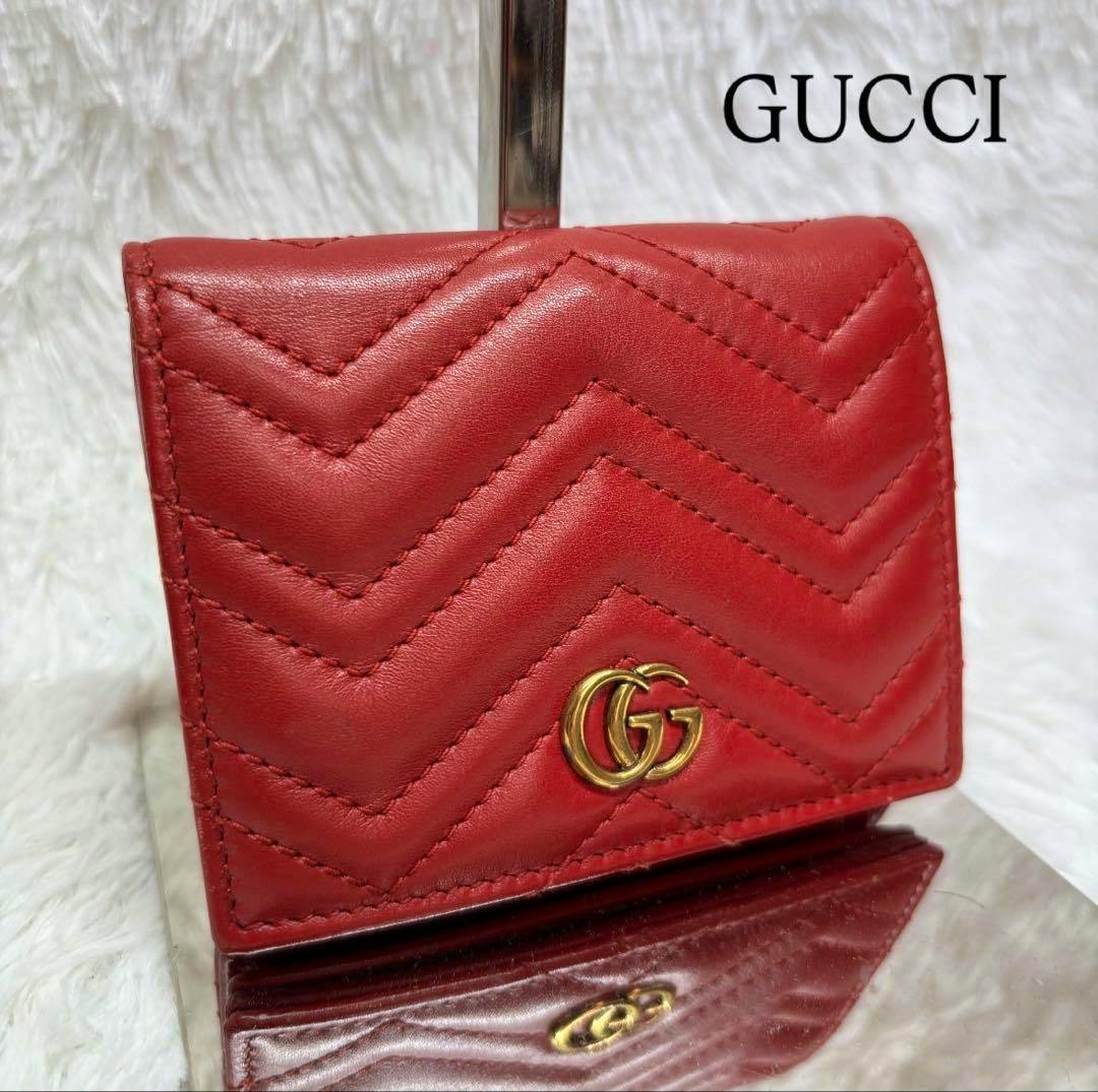 Red quilted Gucci Marmont leather bifold wallet front with a gold GG logo displayed on a reflective surface.