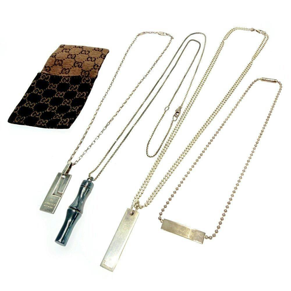 Four necklaces with different pendants laid flat next to a Gucci-branded pouch.