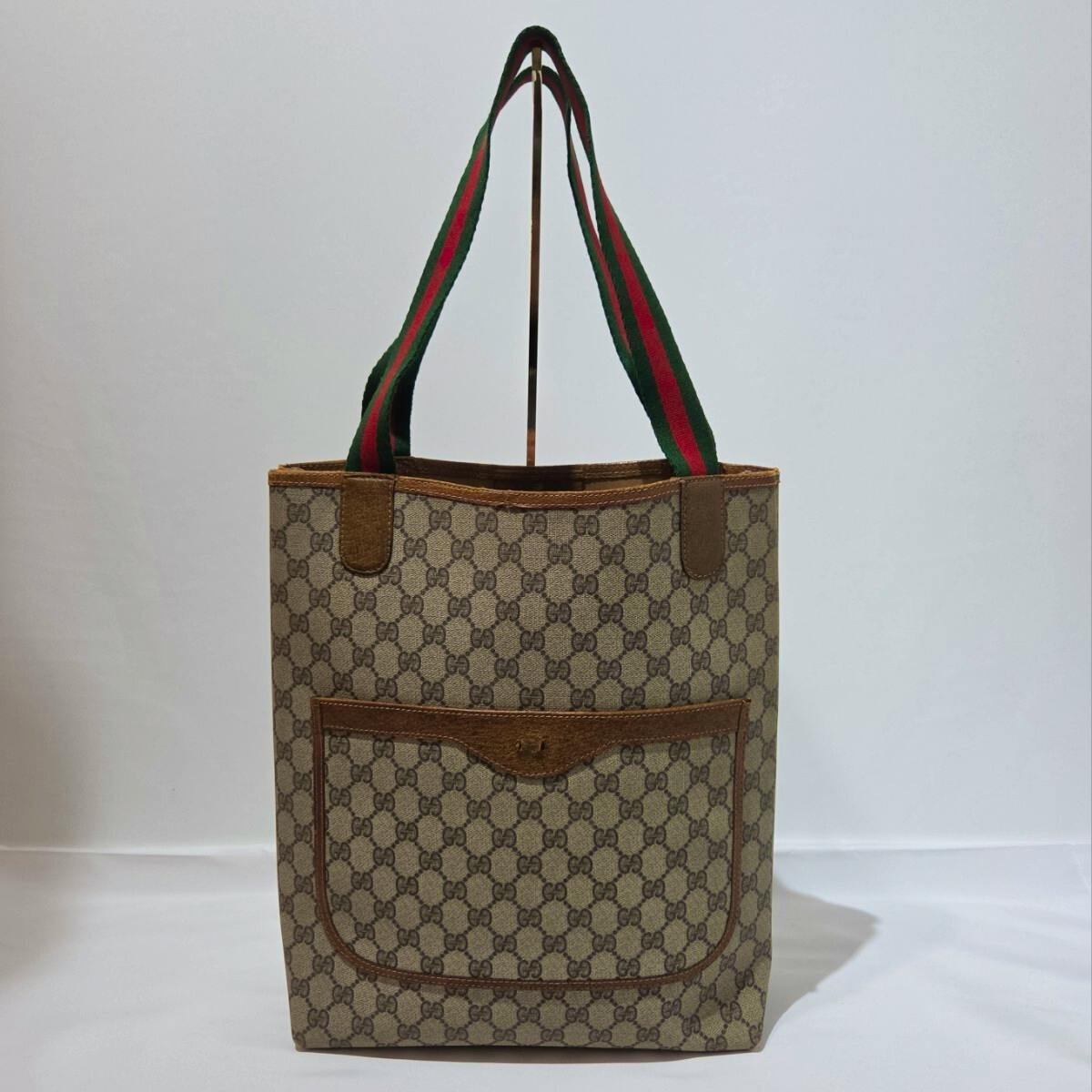 Front view of a GUCCI GG Supreme canvas tote bag with brown leather trim and signature green-red-green shoulder straps.