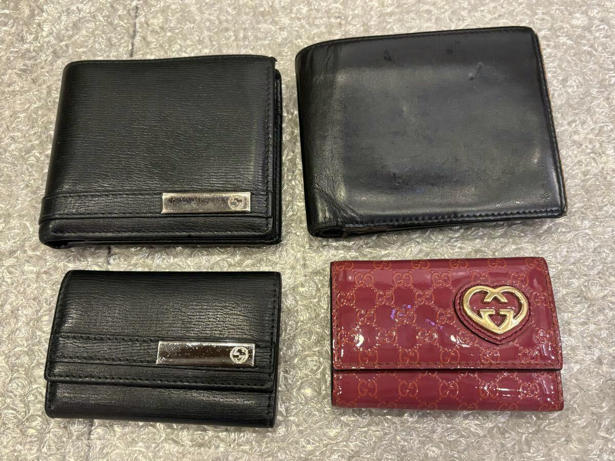 Four wallets laid on bubble wrap: three black leather wallets and one red GG-pattern Gucci wallet.