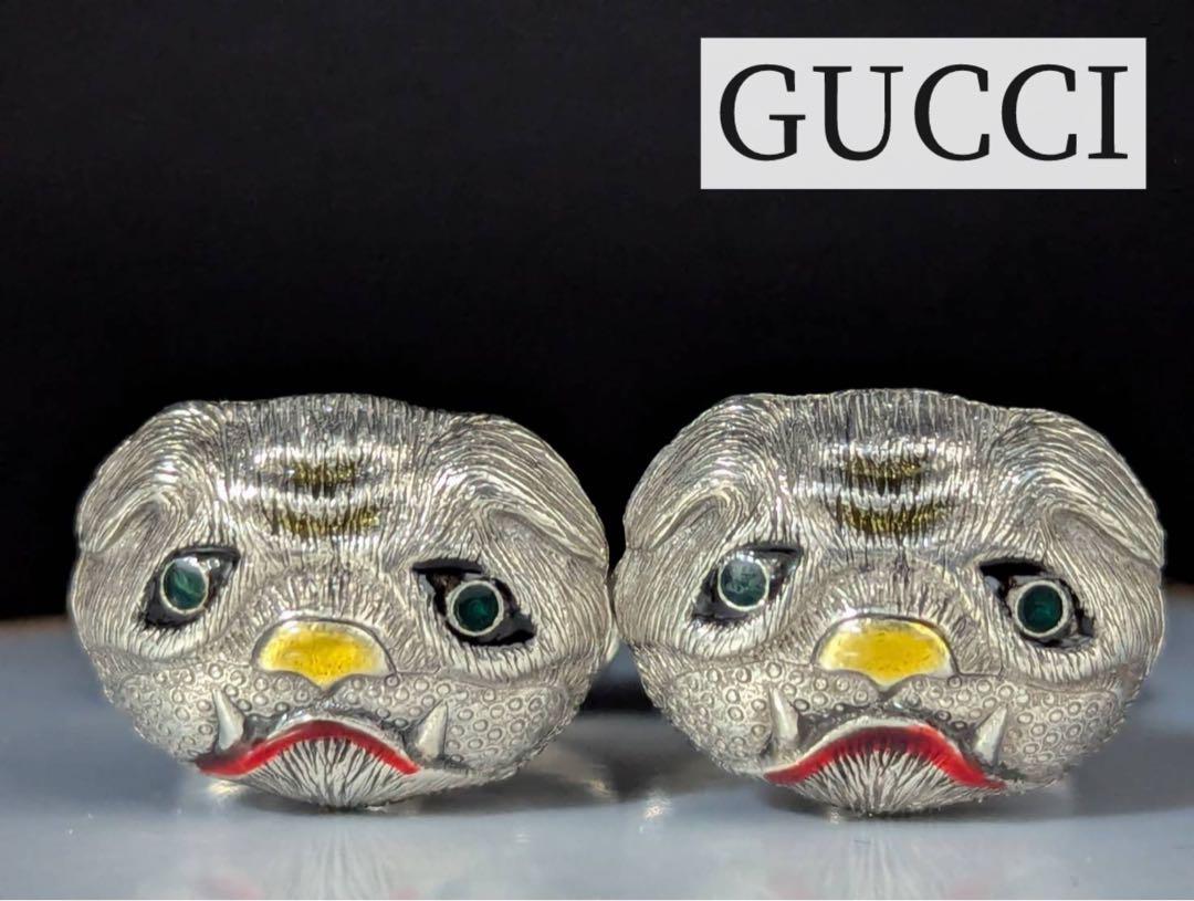 Close-up photo of a pair of silver Gucci pug-shaped cufflinks with painted yellow noses, green eyes, and red mouths.