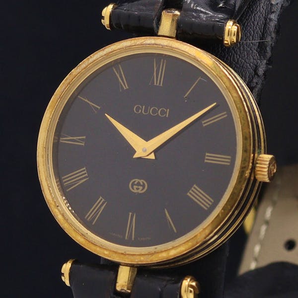 Front view of a Gucci men's wristwatch showing a black dial with gold-tone Roman numerals and gold hands.