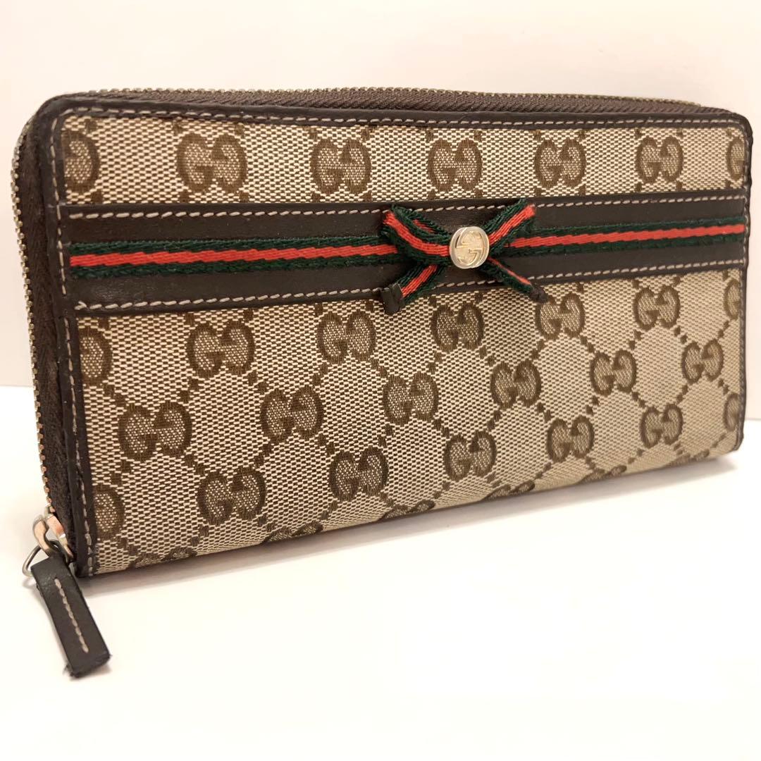 Brown Gucci long zip-around wallet in GG canvas with green-red-green stripe and bow ribbon on the front.