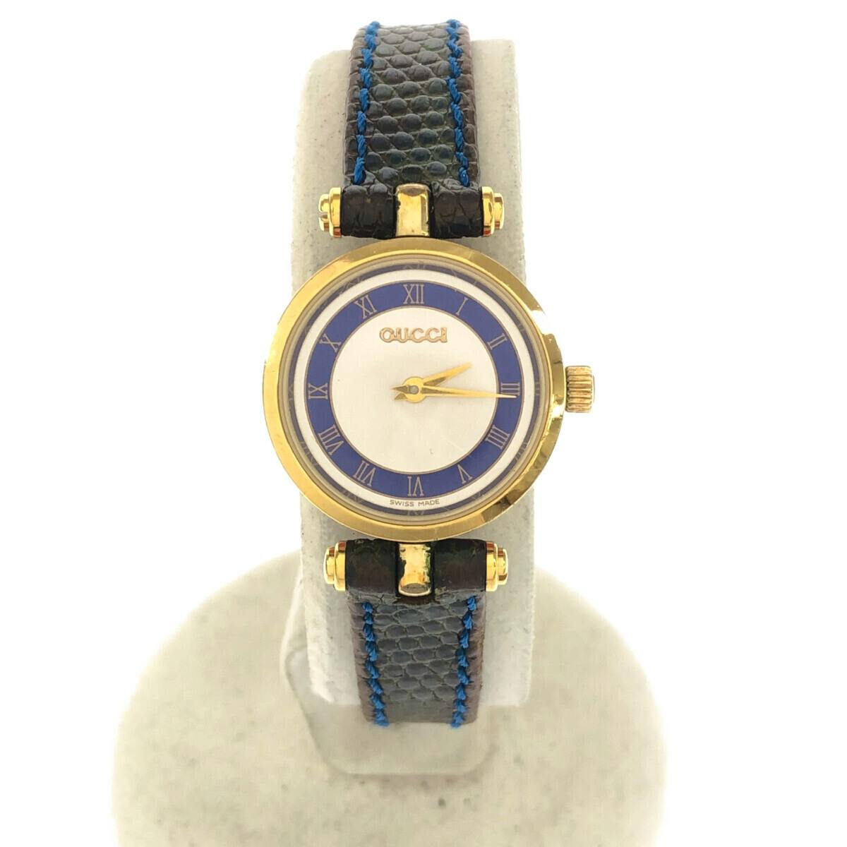 Front view of the GUCCI wristwatch with a blue bi-color dial mounted on a display stand.