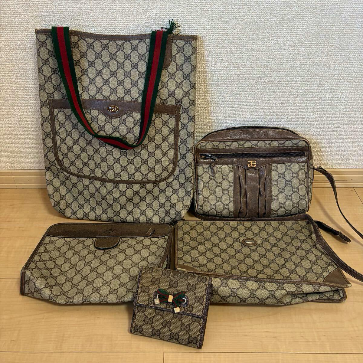 Five Gucci GG canvas pieces arranged on the floor: a tote bag with green-red straps, a shoulder/crossbody bag, two flat pouch-style bags, and a small wallet.
