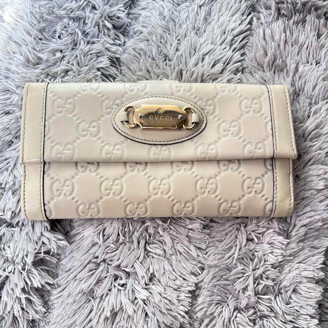 Front view of a white Gucci Sima cow leather long wallet with embossed GG pattern and a metal logo plaque.