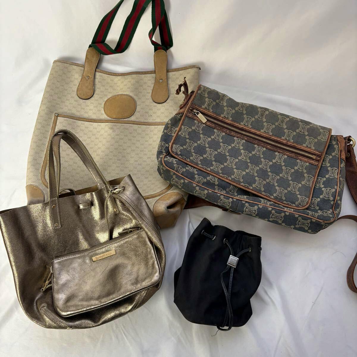 Four bags arranged on a white background: a beige tote with green-red straps, a patterned shoulder bag, a metallic gold tote, and a small black drawstring bag.
