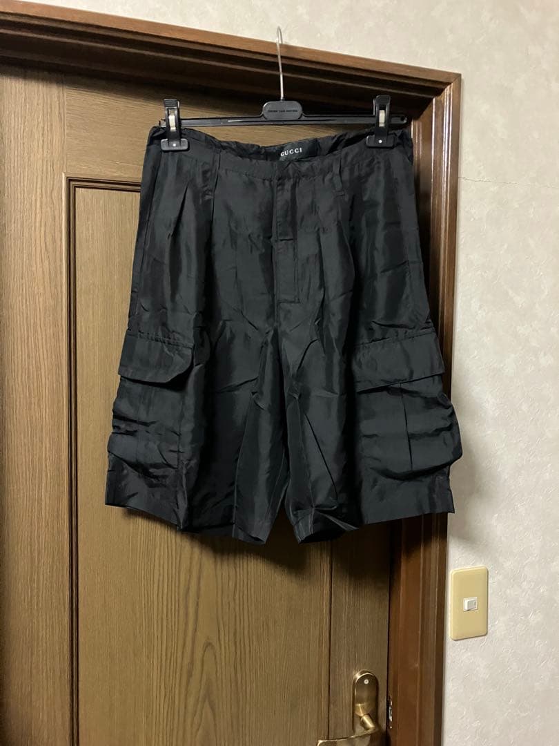 Front view of black silk wide cargo women's shorts hanging on a hanger against a wooden door.