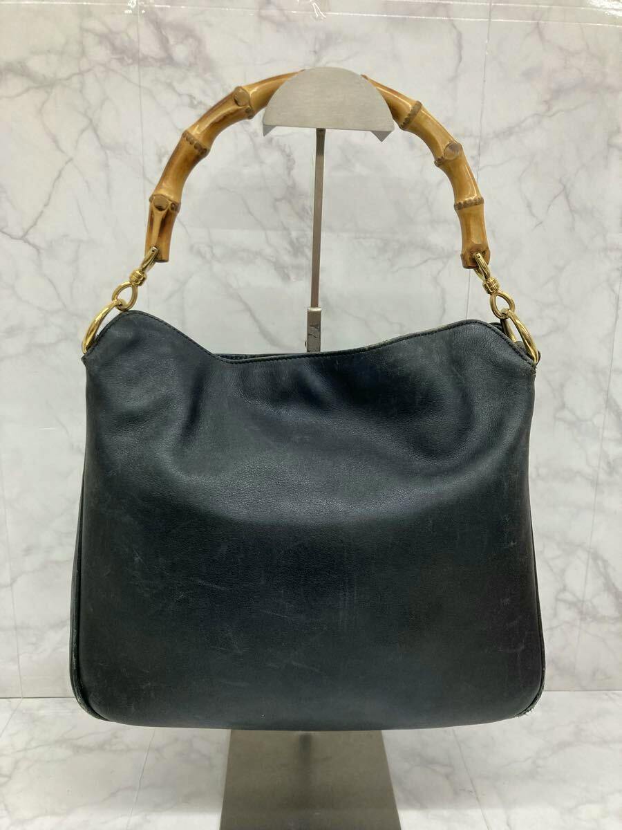 Front view of a black GUCCI leather shoulder handbag with a bamboo handle and gold hardware displayed on a stand.