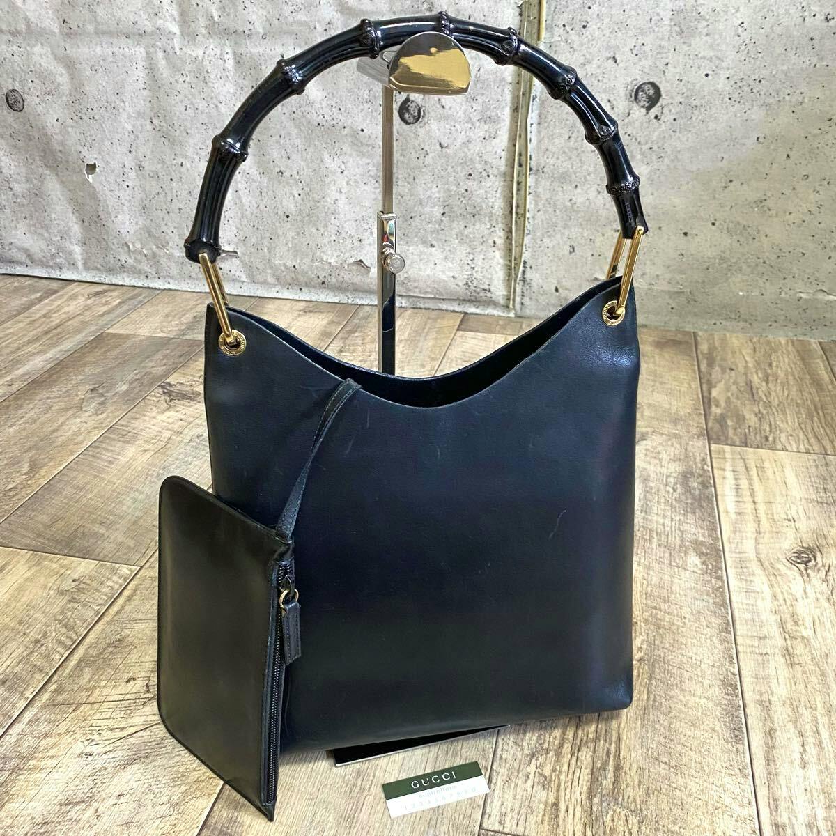 Black GUCCI cow leather bamboo-handle one-shoulder handbag with pouch on a wooden floor.
