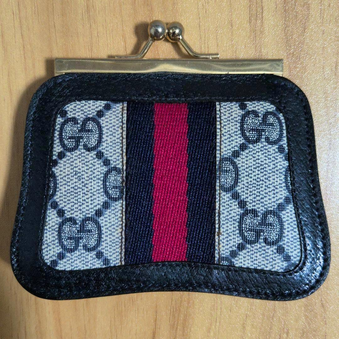 Front view of the GUCCI canvas coin case showing black leather trim, a red-and-blue center web, and a metal kiss‑lock closure.