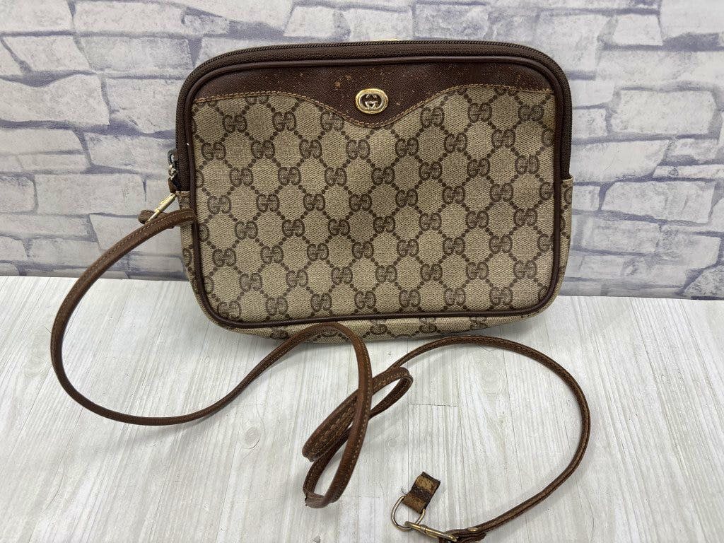 Front view of the GUCCI GG canvas shoulder bag in brown with its long leather strap laid out on a light wood surface.