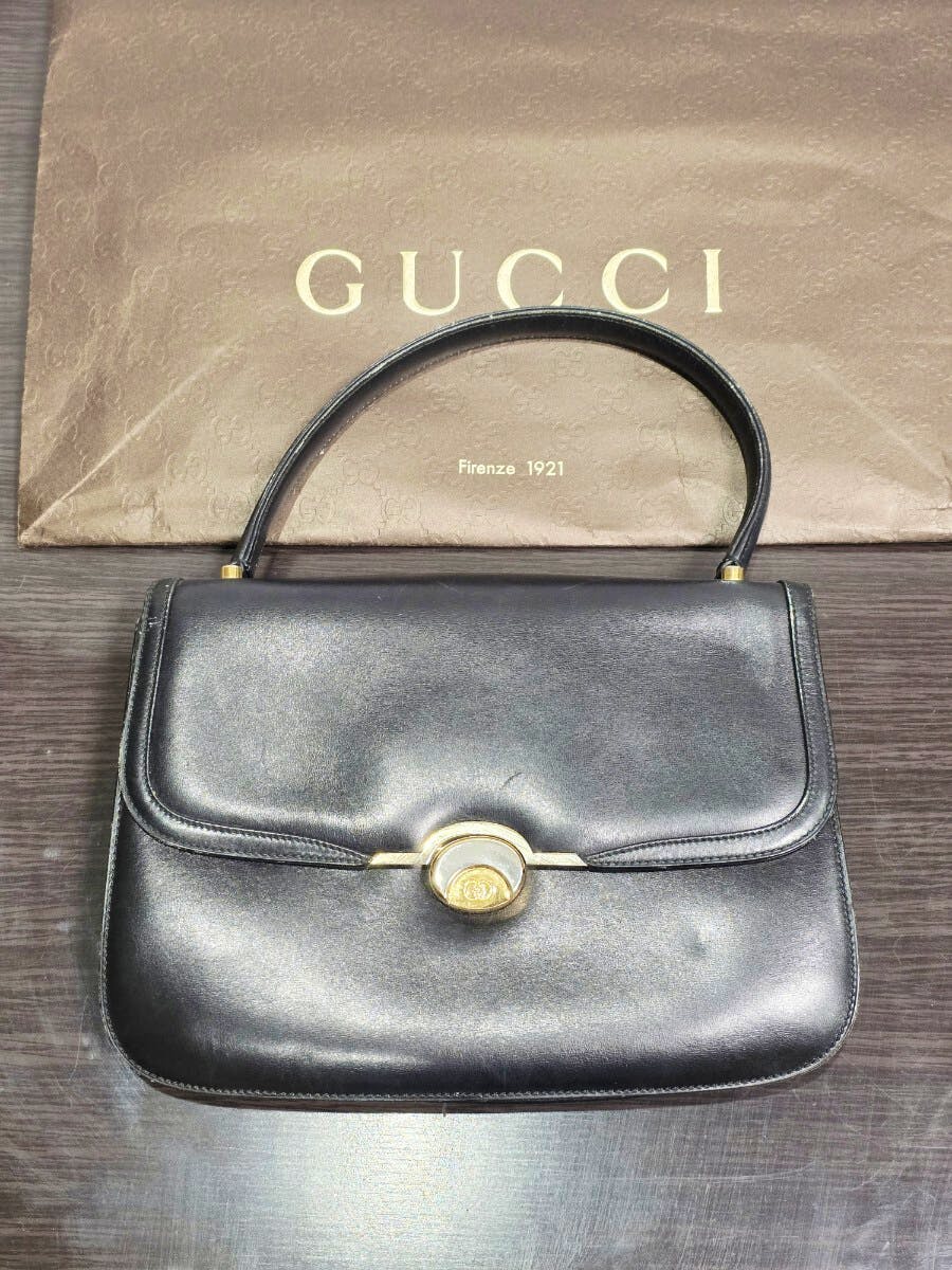 Front view of a black Gucci vintage leather handbag with a top handle and gold turn-lock clasp placed on a GUCCI dust bag.