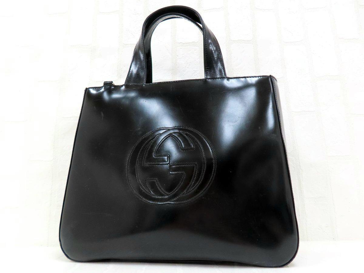 Black patent leather Gucci tote handbag with an embossed double-G logo and two top handles.