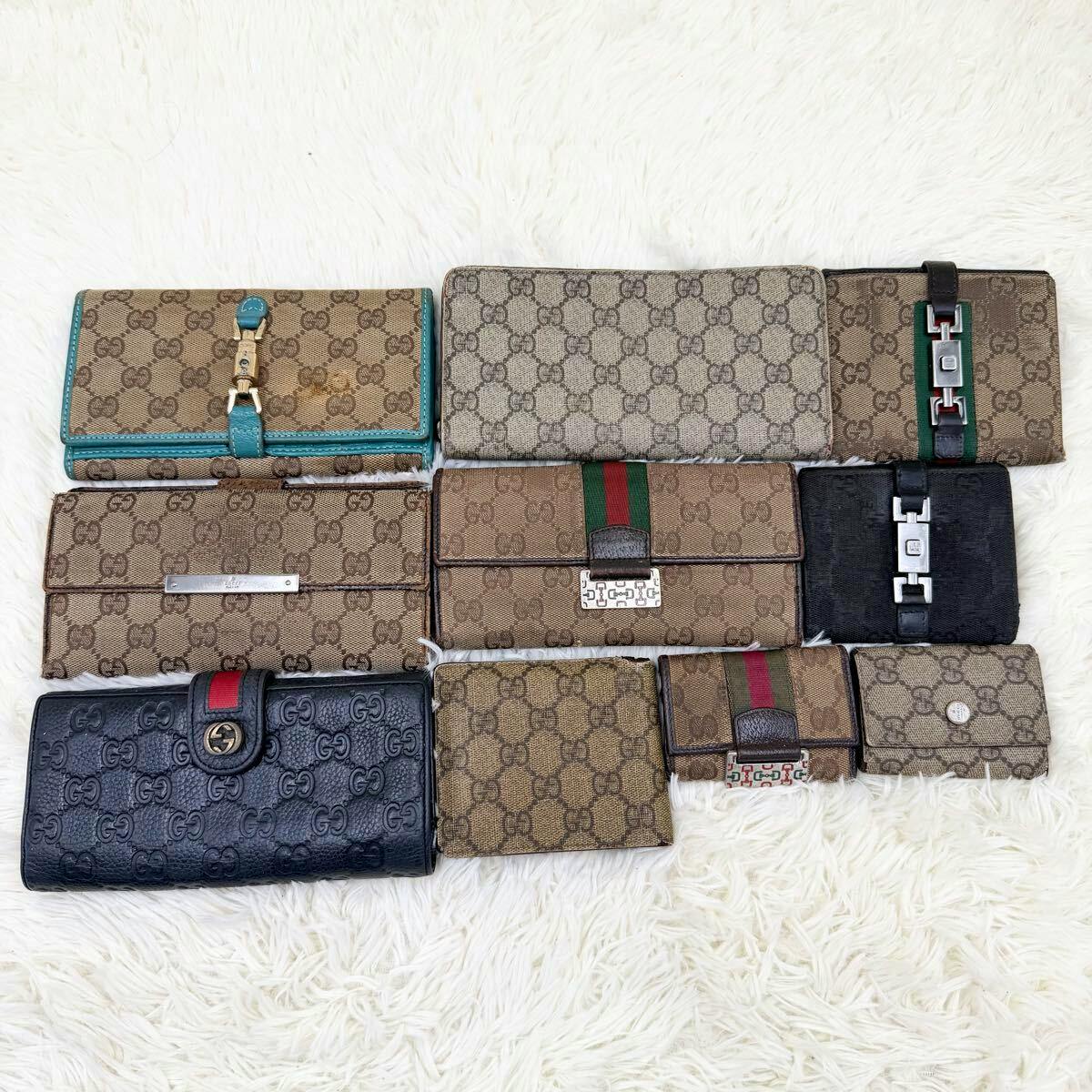 Ten Gucci wallets and small coin cases in various GG canvas and leather styles arranged on a white fur background.