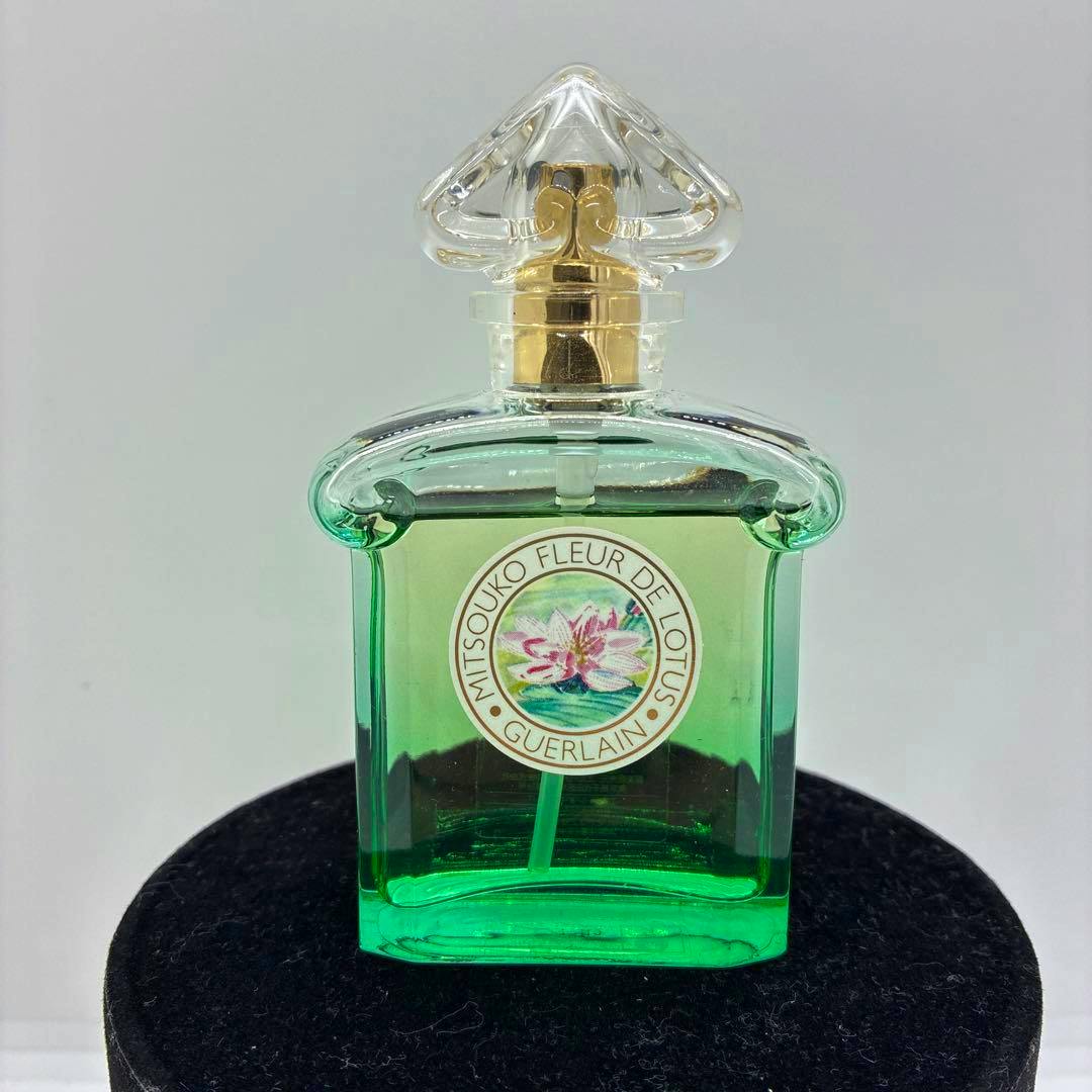 Front view of the GUERLAIN Mitsouko Fleur de Lotus 50ml green glass perfume bottle showing a round lotus label and a clear decorative cap.