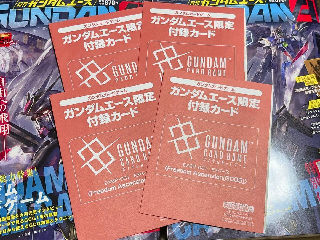 Four red Gundam Ace limited 'GUNDAM CARD GAME' promotional cards laid on top of magazines.