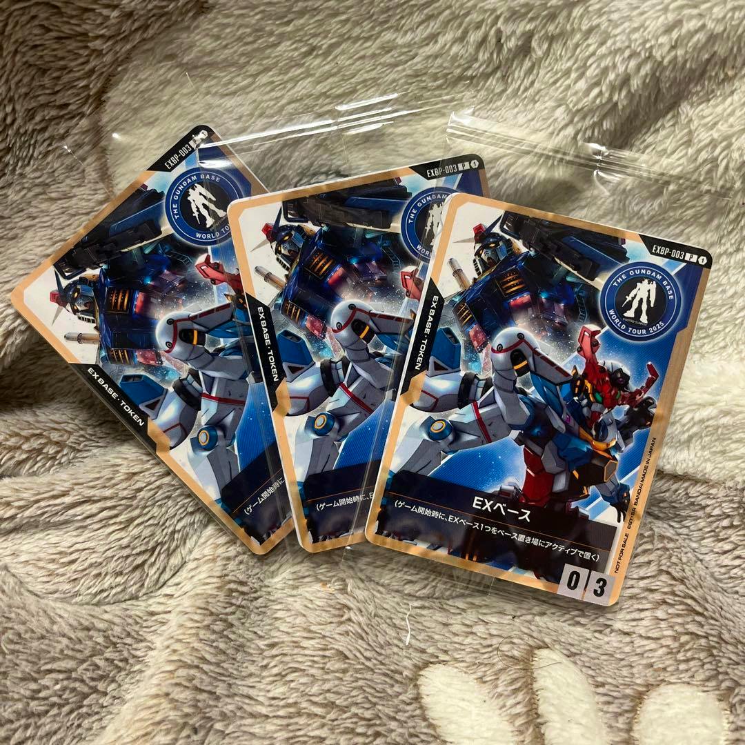 Three ガンダムベース大阪 EXベースカード trading cards showing the front artwork of Gundam mobile suits laid on a blanket.