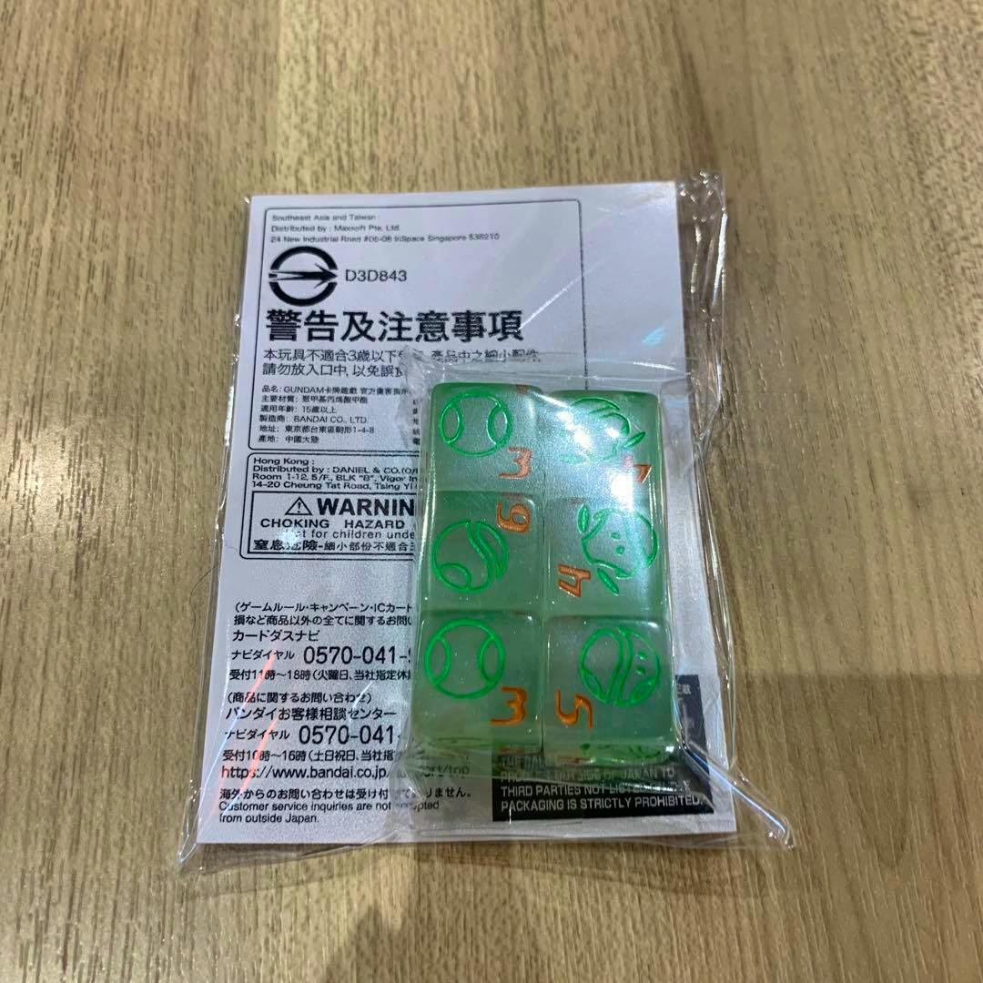 Sealed pack of six translucent green Haro dice in plastic packaging placed on a wooden surface with warning label visible.
